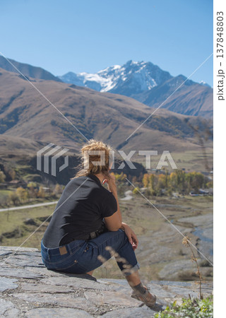 Young Woman Sitting on Stone Looking at Snow Capped Mountain Peak with Copy Space Young Woman Sitting on Stone Looking at Snow Capped Mountain Peak with Copy Space 137848803