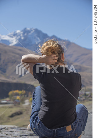 Young Woman Traveler Fixing Hair and Looking at Snow Capped Mountain Peak with Copy Space 137848804