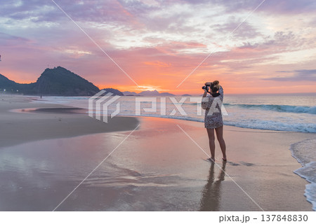Young Female Photographer Taking Photos of Pink Sunrise on Ocean Beach with Copy Space Young Female Photographer Taking Photos of Pink Sunrise on Ocean Beach with Copy Space 137848830