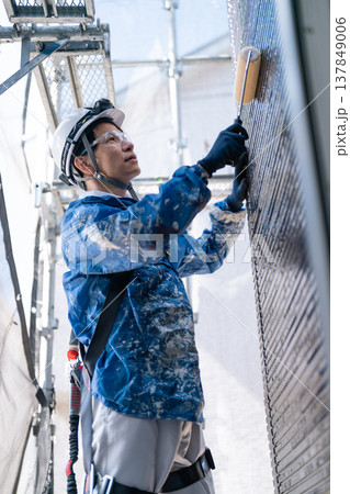 外壁塗装の現場で作業する男性職人。ペンキの付いた作業着で誠実に塗り替えるシーン 137849006