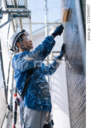 外壁塗装の現場で作業する男性職人。ペンキの付いた作業着で誠実に塗り替えるシーン 137849007