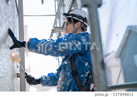 外壁塗装の現場で作業する男性職人。ペンキの付いた作業着で誠実に塗り替えるシーン 外壁塗装の現場で作業する男性職人。ペンキの付いた作業着で誠実に塗り替えるシーン 137849011