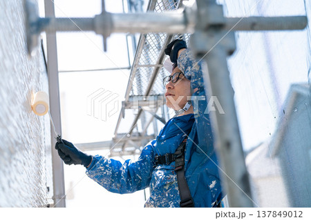 外壁塗装の現場で作業する男性職人。ペンキの付いた作業着で誠実に塗り替えるシーン 137849012