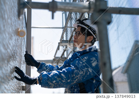 外壁塗装の現場で作業する男性職人。ペンキの付いた作業着で誠実に塗り替えるシーン 外壁塗装の現場で作業する男性職人。ペンキの付いた作業着で誠実に塗り替えるシーン 137849013