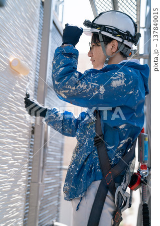 外壁塗装の現場で作業する男性職人。ペンキの付いた作業着で誠実に塗り替えるシーン 137849015