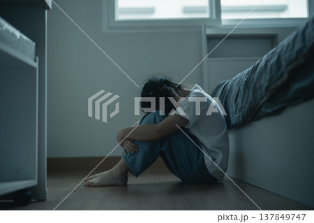 Somber Mood of a Young Girl Sitting Alone on a Floor in a Calm and Minimalist Bedroom Space, Evoking Feelings of Loneliness and Reflection 137849747