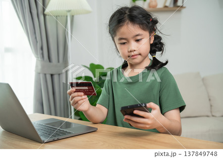 Young girl using smartphone and credit card for online shopping in cozy indoor environment, focus on technology and convenience for kids 137849748