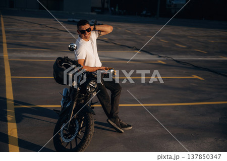 Looking to the side and posing. Man is outdoors with his motorcycle Looking to the side and posing. Man is outdoors with his motorcycle 137850347
