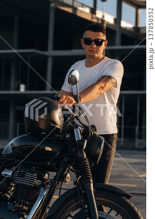 Construction site behind, posing. Man is outdoors with his motorcycle Construction site behind, posing. Man is outdoors with his motorcycle 137850352