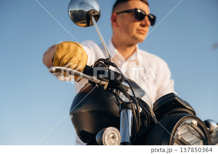White shirt, black sunglasses. Man is outdoors with his motorcycle 137850364