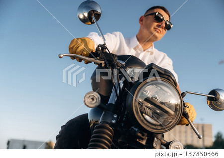 White shirt, black sunglasses. Man is outdoors with his motorcycle 137850366