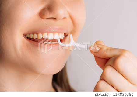 Woman using floss pick between teeth, close up oral care routine 137850380