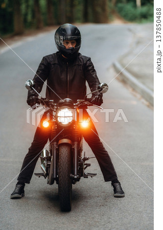 Front view. Man in leather clothes on motorcycle is on the road Front view. Man in leather clothes on motorcycle is on the road 137850488