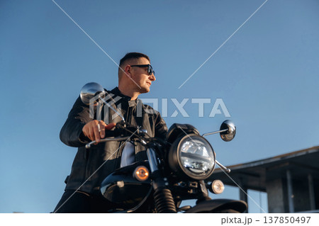 Against clear sky, in sunglasses. Man is outdoors with his motorcycle 137850497