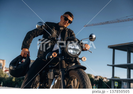 Against clear sky, in sunglasses. Man is outdoors with his motorcycle Against clear sky, in sunglasses. Man is outdoors with his motorcycle 137850505
