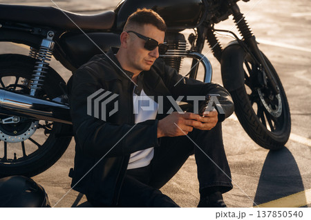 Sitting on the ground. Man is outdoors with his motorcycle Sitting on the ground. Man is outdoors with his motorcycle 137850540