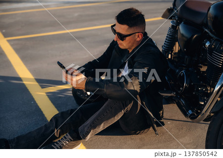 Sitting on the ground. Man is outdoors with his motorcycle 137850542