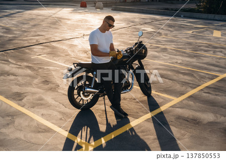 Yellow gloves are on hands, under sunlight. Man is outdoors with his motorcycle Yellow gloves are on hands, under sunlight. Man is outdoors with his motorcycle 137850553