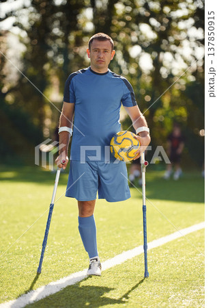 Holding soccer ball. Disabled man with crutches is on the field Holding soccer ball. Disabled man with crutches is on the field 137850915