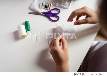 kid hands sew white fabric with needle and thread on light table with purple scissors and spools crafting hobby diy creative project handmade concept kid hands sew white fabric with needle and thread on light table with purple scissors and spools crafting hobby diy creative project handmade concept 137851628