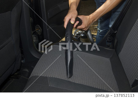 a man vacuums the fabric seat of a car 137852113
