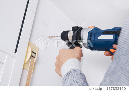 a man drills a hole in a wall with a drill 137852120