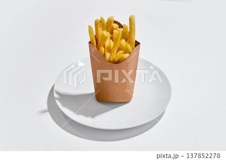 French fries served in paper box placed on white plate on clean white background. 137852278