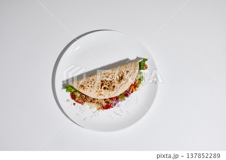 Tortilla wrap filled with vegetables, meat and cheese served on white plate on clean white background top view Tortilla wrap filled with vegetables, meat and cheese served on white plate on clean white background top view 137852289