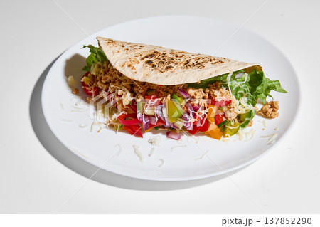Tortilla wrap filled with vegetables, minced meat and melted cheese served on white plate on clean white background Tortilla wrap filled with vegetables, minced meat and melted cheese served on white plate on clean white background 137852290