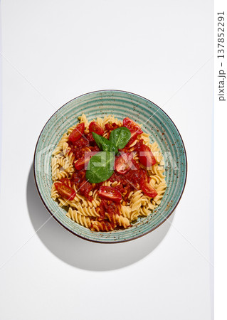Fusilli pasta with tomato sauce, cherry tomatoes and fresh basil served on ceramic plate on white background. 137852291