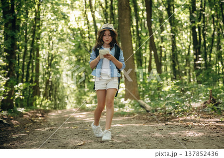 Small notepad is in hands. Young girl hiker is in the forest Small notepad is in hands. Young girl hiker is in the forest 137852436
