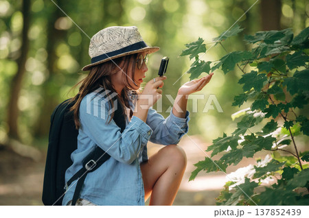 Discovering plants under magnifying glass. Young girl hiker is in the forest 137852439