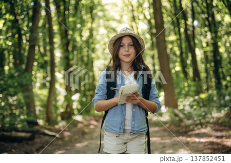 Looking straight into the camera. Young girl hiker is in the forest 137852451