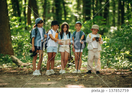 Camera and paper map in hands. Group of children in the forest on a hike Camera and paper map in hands. Group of children in the forest on a hike 137852759