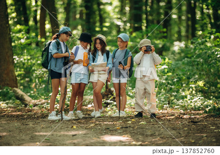 Camera and paper map in hands. Group of children in the forest on a hike 137852760
