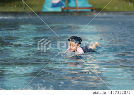 Happy Child Swimming in Clear Water of Swimming Pool During Summer Day Fun with Goggles and Swimwear Happy Child Swimming in Clear Water of Swimming Pool During Summer Day Fun with Goggles and Swimwear 137852873