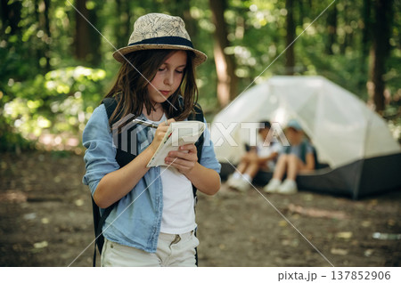 Focused, writing information into notepad. Girls kids are in the forest, hike conception 137852906