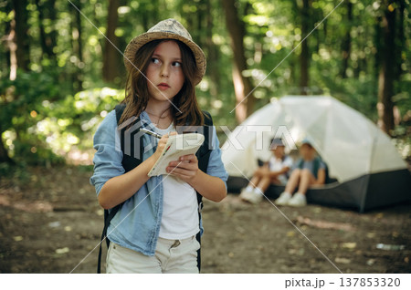 Pen and notepad is in hands. Girls kids are in the forest, hike conception 137853320