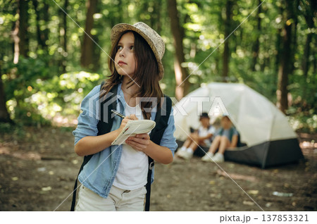 Pen and notepad is in hands. Girls kids are in the forest, hike conception 137853321