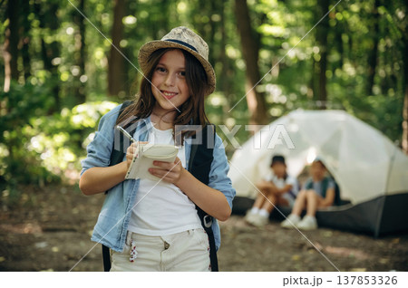 Notepad and pen is in hands. Girls kids are in the forest, hike conception Notepad and pen is in hands. Girls kids are in the forest, hike conception 137853326