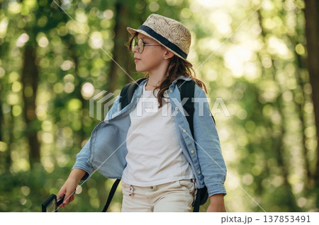 In hat and with backpack. Young girl hiker is in the forest 137853491