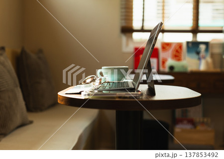 Warm toned home workspace with tablet, coffee cup, and glasses on a small wooden table. 137853492