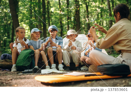 Survival tips, sitting at camp. Woman is doing tour for group of kids in the forest 137853601