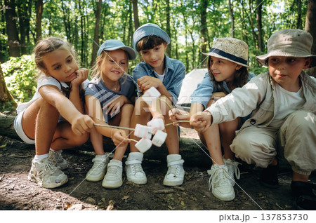 Cheerful, marshmallow time, sitting. Group of children in the forest on a hike Cheerful, marshmallow time, sitting. Group of children in the forest on a hike 137853730