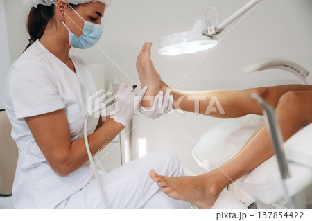 View from the side, doing peeling. Podiatrist with client in clinic 137854422