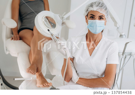 Silver professional peeling equipment. Podiatrist with client in clinic 137854438