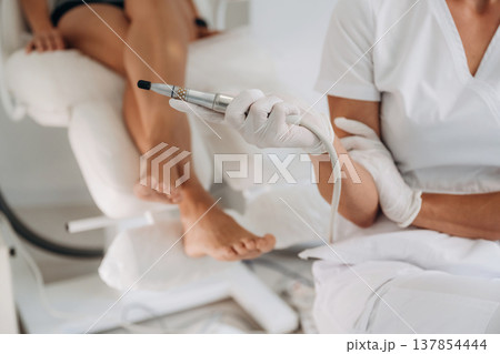 Silver professional peeling equipment. Podiatrist with client in clinic 137854444