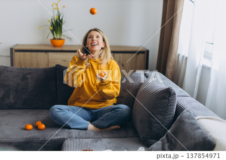 Happy woman tossing tangerines in air enjoying playful healthy lifestyle and joyful energy at home in cozy modern interior 137854971