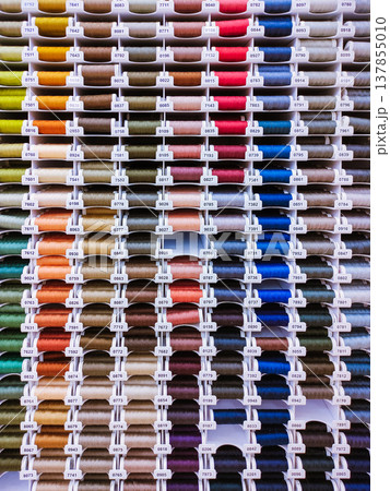Vertical photo with many thread spools arranged in even rows. Bright image for sewing, tailoring, craft, atelier and textile supply themes. 137855010