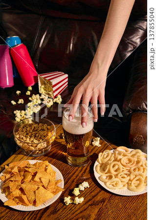 Hand grabbing beer glass with snacks and popcorn on wooden table with copy space. Hand grabbing beer glass with snacks and popcorn on wooden table with copy space. 137855040